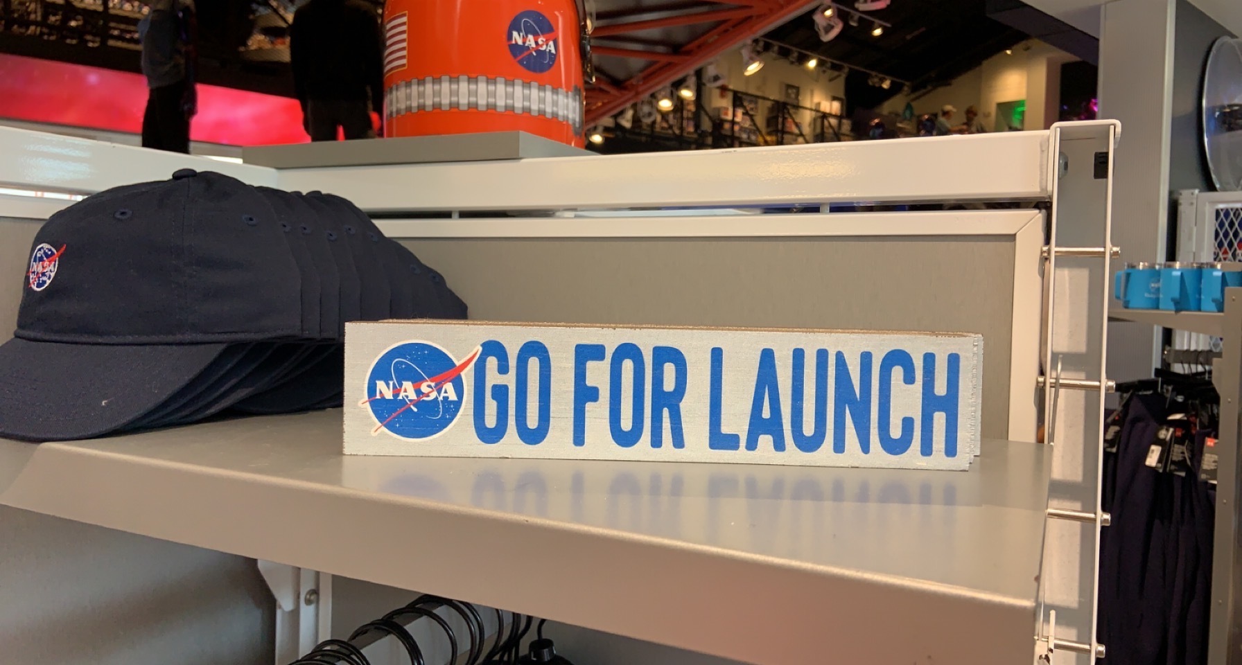 A wooden sign reading GO FOR LAUNCH with the NASA logo, on a gift shop shelf